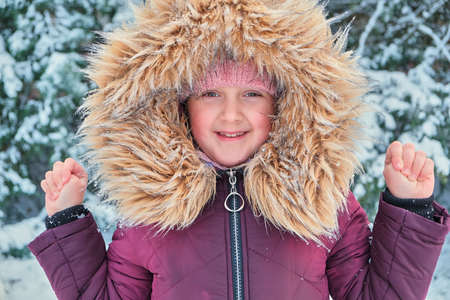 Happy laughing toddler girl wearing a fur jacket while playing in a beautiful snow dayの写真素材