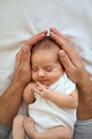 Close-up of unrecognizable father holding head of sleeping baby, sleeping in a bed. In the safe handsの写真素材