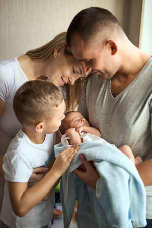 Father and mother holding newborn daughter in arms, older brother stands next to and looks with love. family valuesの写真素材