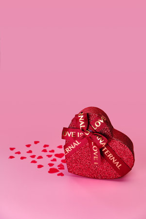 Valentines day greeting card with gift box in the shape of a heart, in front of pink background with hearts and space for your greetingsの写真素材