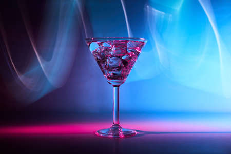 Martini cocktail drink with ice cubes in neon iridescent pink and blue colors. Minimal night party life and Juzz concept. Background painted with lightの写真素材