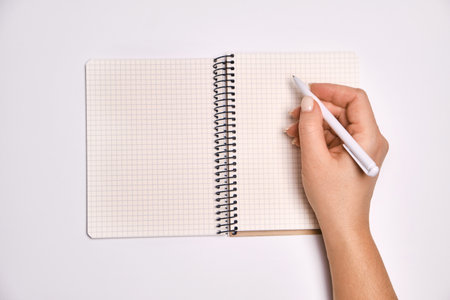 Woman's hand holding pen and open spiral notebook with blank white pages, on light white background....