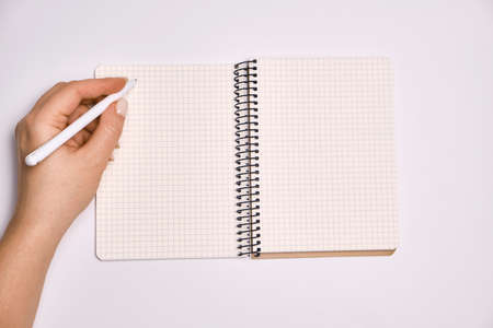 Woman's hand holding pen and open spiral notebook with blank white pages, on light white background. planning conceptの写真素材
