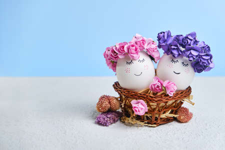Two cuddling Easter eggs with sweet faces with floral spring wreaths lying in a cozy Easter basket. Creative postcard for Easter with copy spaceの写真素材