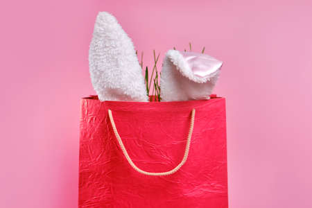 Easter bag with Easter decor. Bunny ears, eggs and fresh green grass on a pink background with copy...