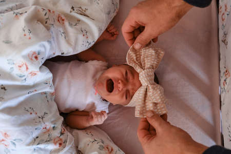 Hands of a caring father put a newborn baby lying in a baby bed with a bow. Top view, close up, selective focus.の写真素材