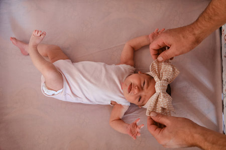 Hands of a caring father put a newborn baby lying in a baby bed with a bow. Top view, close up, selective focus.の写真素材