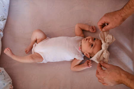 Hands of a caring father put a newborn baby lying in a baby bed with a bow. Top view, close up,...