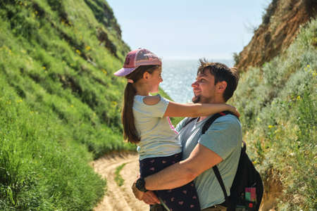 Cropped image of happy father and daughter in green hills. Family walking, hugging, dad carrying little girl. Leisure, family time, parenting conceptの写真素材