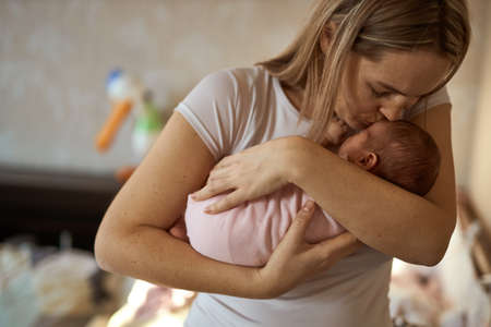 Close-up of happy young mother holding head newborn baby and kissing her sweet adorable newborn...