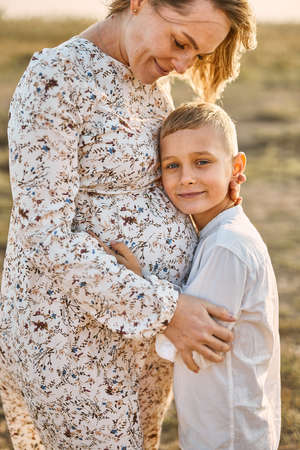 Small boy hugging belly of his pregnant mother outdoors at summerの写真素材