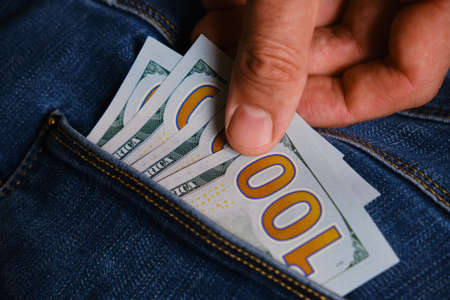 hand takes US dollar banknote from the right front pocket of blue jeans. Concept of saving money or pocket expensesの写真素材