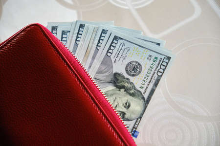 Red wallet full of money on wooden table - one hundred US banknotes with president Franklin...