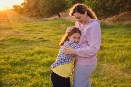 Side view on cheerful mother and daughter hugging each other, playing in the park on green grass in spring sunny day, happy family lifeの写真素材