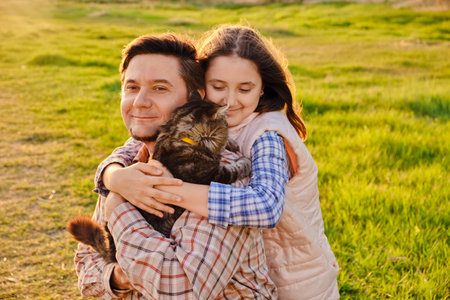 A happy father is having fun with his little daughter holding a fluffy domestic cat outdoor in park, the daughter is hugging her dad and catの写真素材