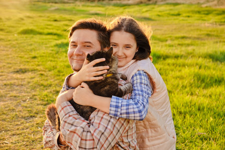 A happy father is having fun with his little daughter holding a fluffy domestic cat outdoor in park, the daughter is hugging her dad and catの写真素材