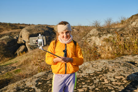 Shot of a kid girl talking on camera in hills, make video blog use device make video hold hand social network blog. child vlogger filming video diary outdoors. kid creating social media content.の写真素材