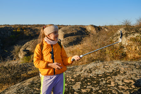 Shot of a kid girl talking on camera in hills, make video blog use device make video hold hand social network blog. child vlogger filming video diary outdoors. kid creating social media content.の写真素材