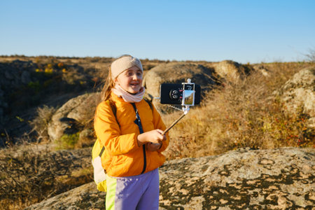 Shot of a kid girl talking on camera in hills, make video blog use device make video hold hand social network blog. child vlogger filming video diary outdoors. kid creating social media content.の写真素材