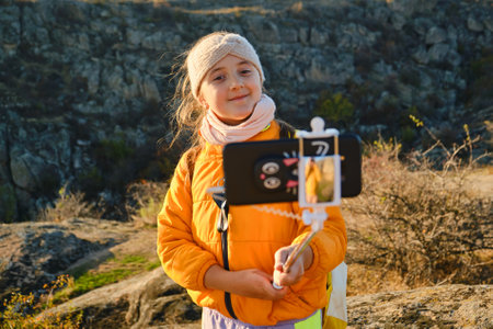 Shot of a kid girl talking on camera in hills, make video blog use device make video hold hand social network blog. child vlogger filming video diary outdoors. kid creating social media content.の写真素材