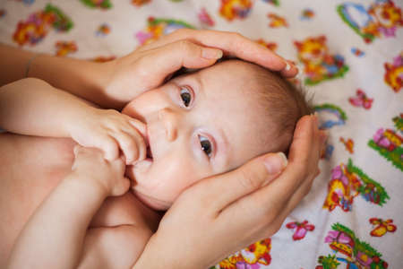Mother holding head of her newborn daugther in hands. The baby on hands at mum. Loving mother hand holding cute smiling newborn baby childの写真素材