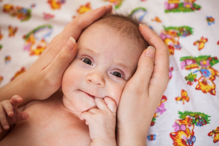 Mother holding head of her newborn daugther in hands. The baby on hands at mum. Loving mother hand holding cute smiling newborn baby childの写真素材