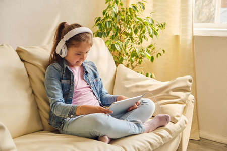 Cute little girl in casual clothes and headphones using a tabletの写真素材