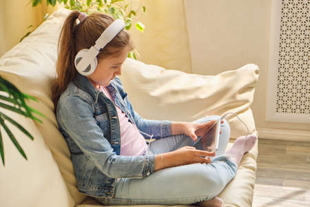 Cute little girl in casual clothes and headphones using a tabletの写真素材