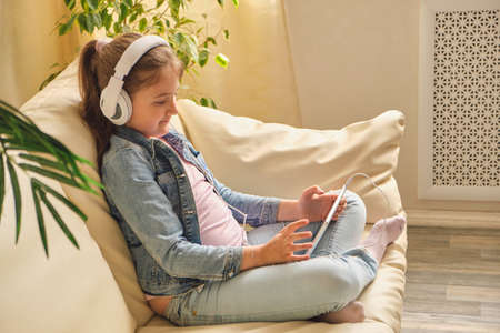 Cute little girl in casual clothes and headphones using a tabletの写真素材