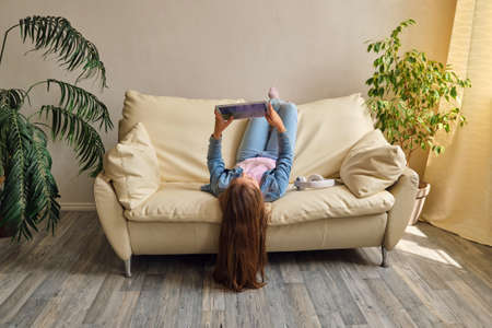 little girl lying upside down on sofaの写真素材