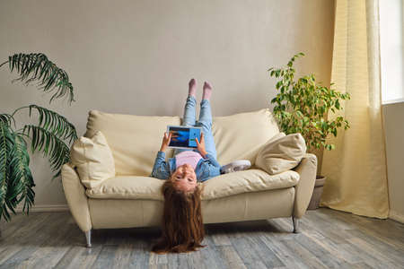little girl lying upside down on sofaの写真素材