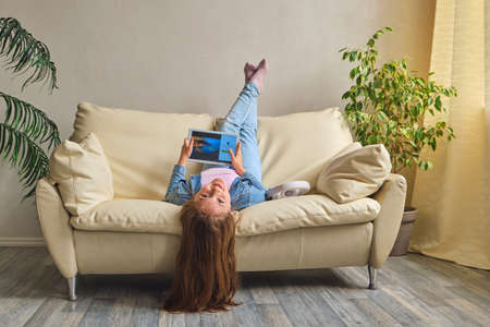 little girl lying upside down on sofaの写真素材