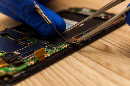 The technician repairing the smartphones motherboard in the workshop on the table.の写真素材