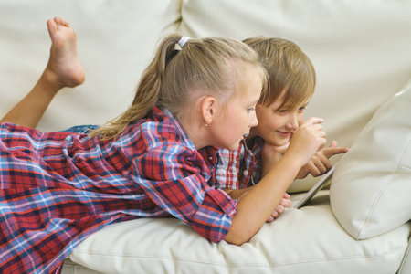 smiling brother and sister with tablet on the sofa in living roomの写真素材