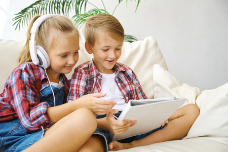 Cute kids with headphones enjoying tablet at home.