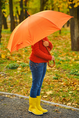 Funny unrecognizable kid under an orange umbrellaの写真素材