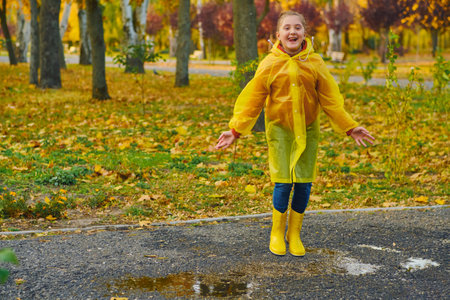 A happy girl in a yellow raincoat and rubber boots on an autumn walk.の写真素材