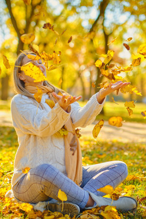 young woman throw leaves in a park in autumnの写真素材