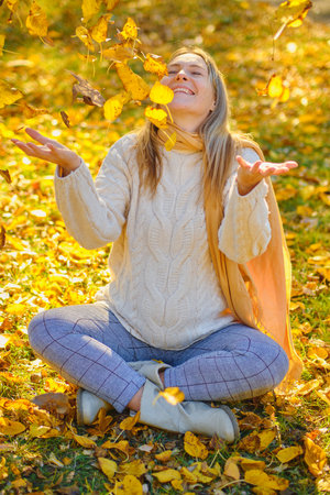 young woman throw leaves in a park in autumnの写真素材