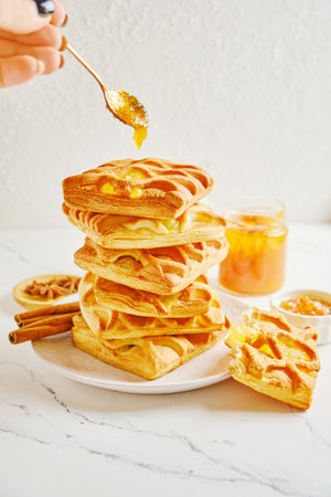 Womans hand puts a spoon of citrus jam on stack of puff pastryの写真素材