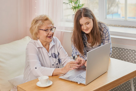 Adult granddaughter teaching her elderly grandmother to use laptopの写真素材