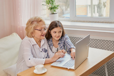 Adult granddaughter teaching her elderly grandmother to use laptop