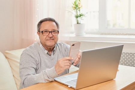 Cheerful senior man has phone conversation at homeの写真素材