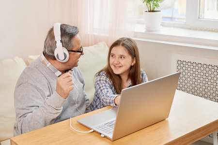 Granddaughter helping grandpa to make on line communication on laptopの写真素材