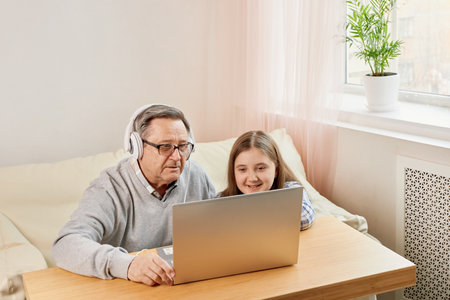 Granddaughter helping grandpa to make on line communication on laptopの写真素材