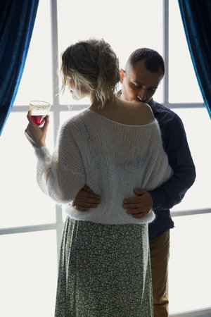 Stylish couple embracing in the dramatic lighting of a glowing windowの写真素材