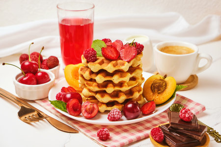 Belgian waffles with strawberries, apricots, cherries, juice and a cup of black coffeeの写真素材