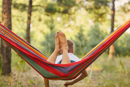 Cute little boy having fun with multicolored hammock in the backyard. Summer active leisure for kids. child on hammock. Activities and fun for children outdoors. selective focusの写真素材