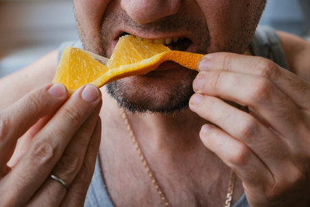 Unrecognizable middle-aged man eating an orange slice, close-upの写真素材
