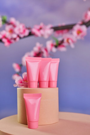 Pink tubes for cosmetics on a round podium and branches of cherry blossoms on a sky backgroundの写真素材